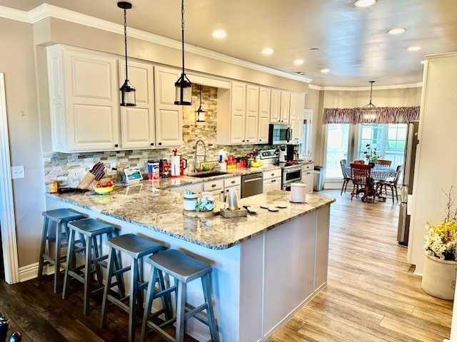 kitchen with light hardwood / wood-style flooring, kitchen peninsula, stainless steel appliances, hanging light fixtures, and sink