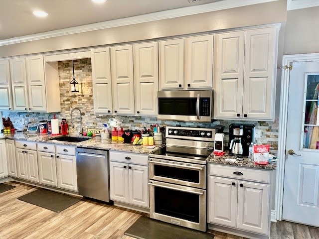 kitchen with appliances with stainless steel finishes, sink, tasteful backsplash, and crown molding