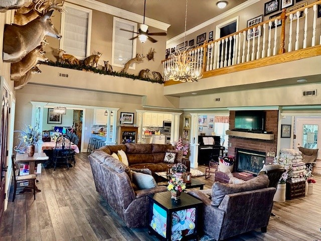 living room with a fireplace, ceiling fan with notable chandelier, a high ceiling, ornamental molding, and hardwood / wood-style flooring