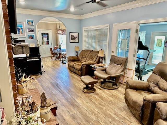 living room featuring light hardwood / wood-style floors, a wealth of natural light, ornamental molding, and ceiling fan with notable chandelier