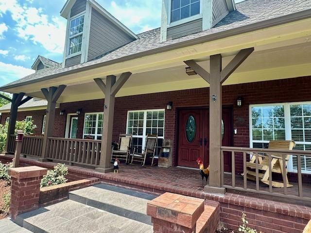 view of exterior entry with covered porch, brick siding, and a shingled roof