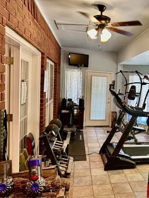 exercise area with ornamental molding, brick wall, light tile flooring, and ceiling fan