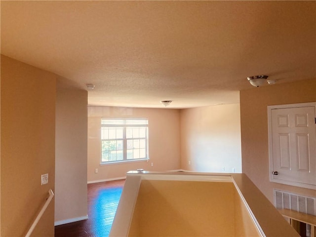 corridor featuring an upstairs landing, visible vents, a textured ceiling, and baseboards