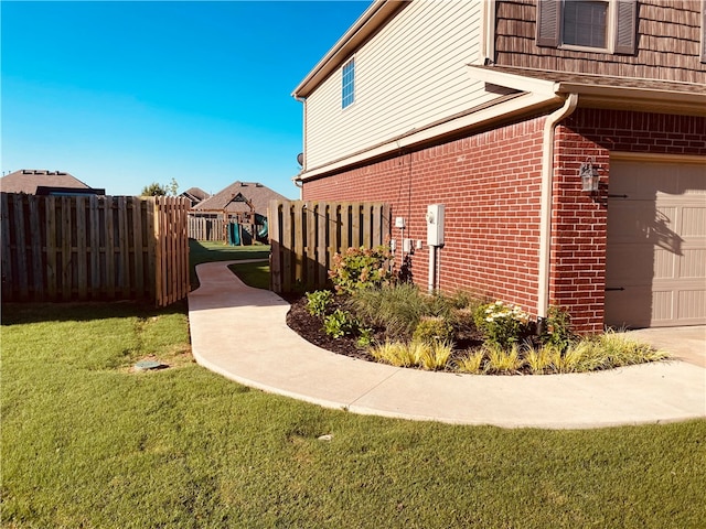 view of side of home featuring a yard, fence, brick siding, and an attached garage