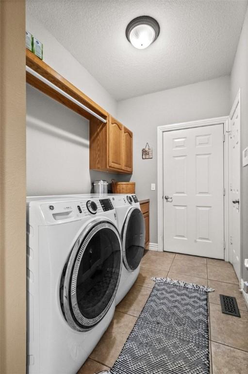 clothes washing area with cabinets, washing machine and dryer, light tile patterned floors, and a textured ceiling