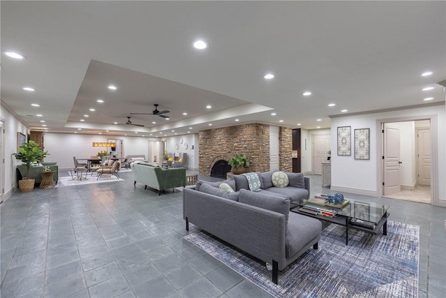 living room featuring ceiling fan, a fireplace, and a tray ceiling