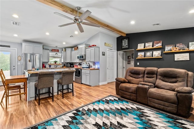 living room featuring ceiling fan, light hardwood / wood-style floors, and vaulted ceiling with beams