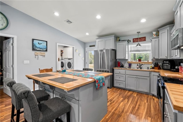 kitchen featuring wood counters, stainless steel appliances, gray cabinets, and washing machine and dryer