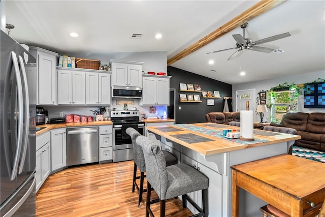 kitchen with a breakfast bar area, appliances with stainless steel finishes, white cabinetry, vaulted ceiling with beams, and wood counters