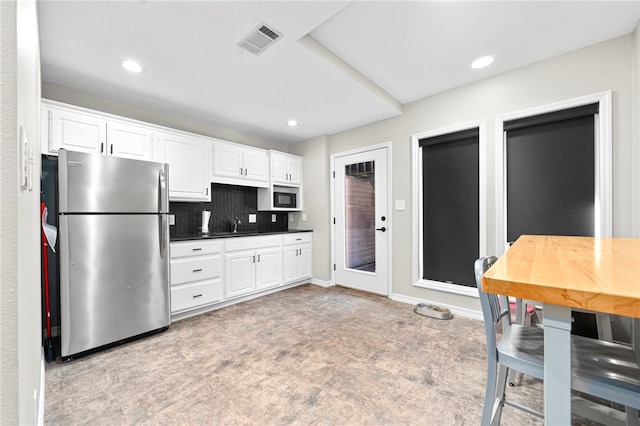 kitchen with freestanding refrigerator, white cabinetry, built in microwave, tasteful backsplash, and dark countertops