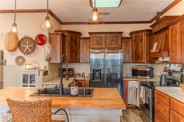 kitchen featuring pendant lighting, hardwood / wood-style flooring, ornamental molding, appliances with stainless steel finishes, and butcher block countertops