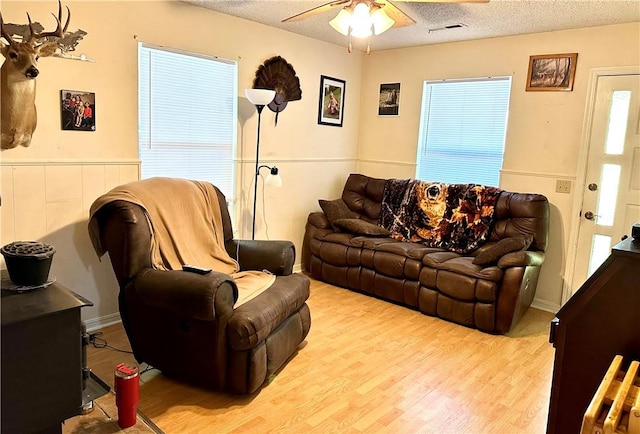 living room with a textured ceiling, ceiling fan, and light hardwood / wood-style floors