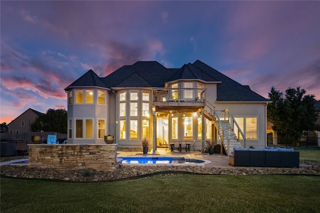 back house at dusk with a yard, an outdoor hangout area, a balcony, and a patio