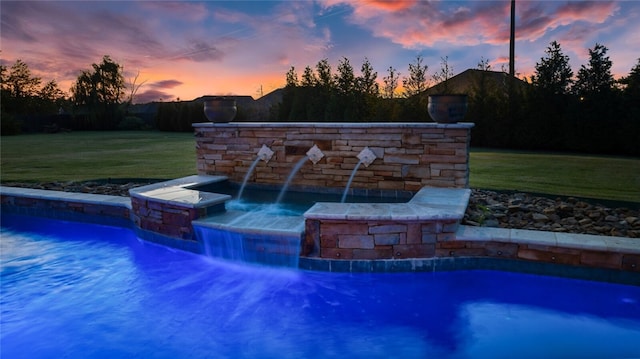 pool at dusk featuring pool water feature and a lawn