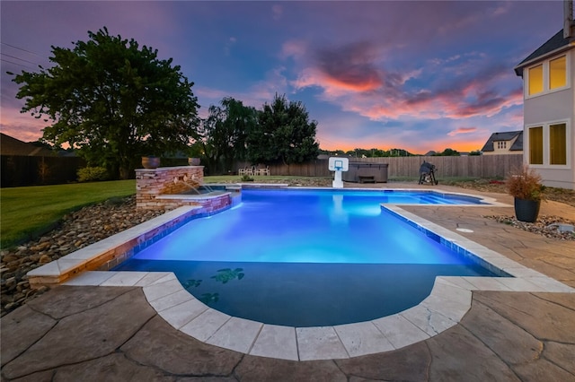 pool at dusk with pool water feature, a patio area, and a hot tub