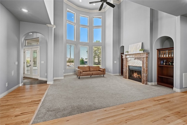 living room featuring ceiling fan, a high ceiling, carpet floors, a fireplace, and ornamental molding