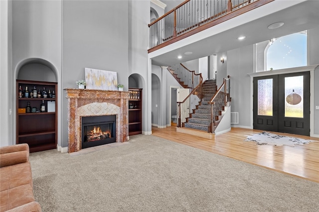 living room with carpet, a towering ceiling, a tile fireplace, and french doors