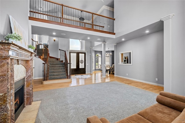 foyer entrance featuring a high ceiling, an inviting chandelier, light hardwood / wood-style flooring, decorative columns, and a fireplace