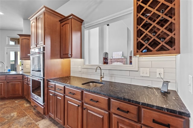 kitchen with dark stone counters, decorative backsplash, sink, and stainless steel double oven