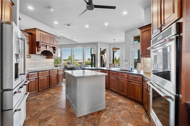 kitchen featuring ceiling fan with notable chandelier, sink, stainless steel refrigerator with ice dispenser, multiple ovens, and kitchen peninsula