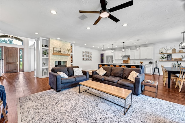 living room featuring a textured ceiling, hardwood / wood-style floors, a stone fireplace, ornamental molding, and ceiling fan