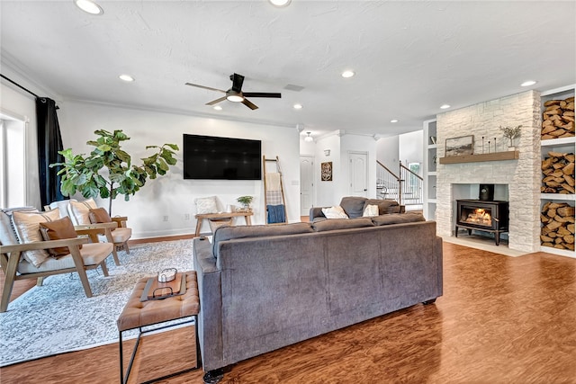 living room with wood-type flooring, a stone fireplace, crown molding, and ceiling fan