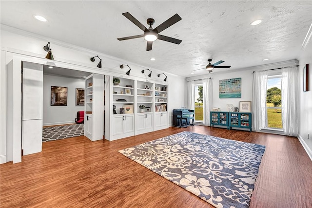 living area featuring a textured ceiling, wood finished floors, a ceiling fan, and ornamental molding