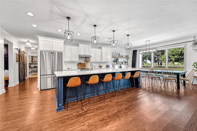 kitchen with stainless steel refrigerator, a large island with sink, pendant lighting, and white cabinets