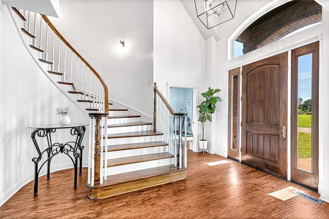 foyer entrance with stairway, baseboards, a chandelier, a high ceiling, and wood finished floors