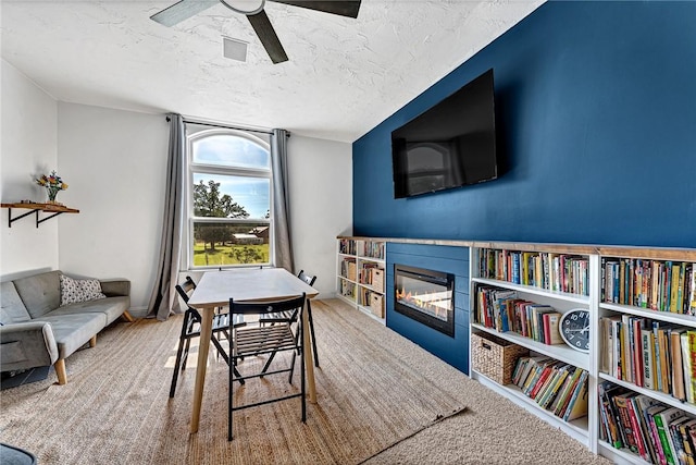 dining area featuring a ceiling fan, carpet floors, a glass covered fireplace, and a textured ceiling