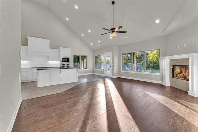 unfurnished living room featuring ceiling fan, sink, a tile fireplace, high vaulted ceiling, and light hardwood / wood-style flooring