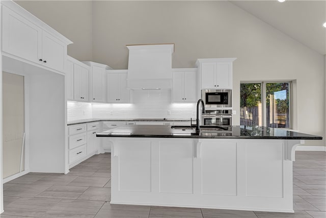 kitchen with stainless steel appliances, sink, high vaulted ceiling, white cabinetry, and an island with sink