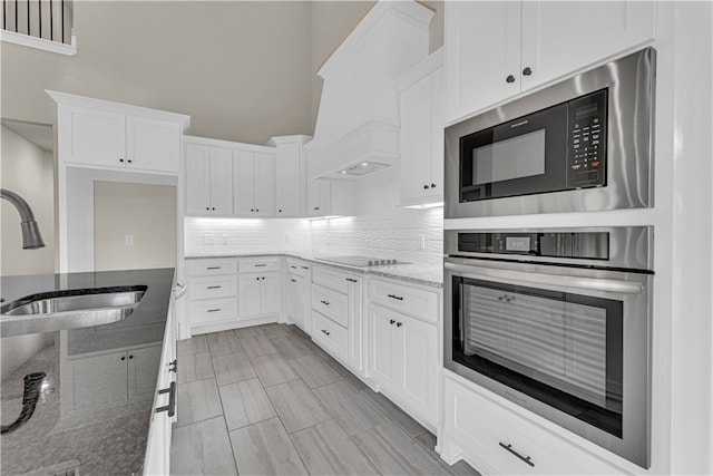 kitchen with built in microwave, stainless steel oven, sink, dark stone counters, and white cabinets