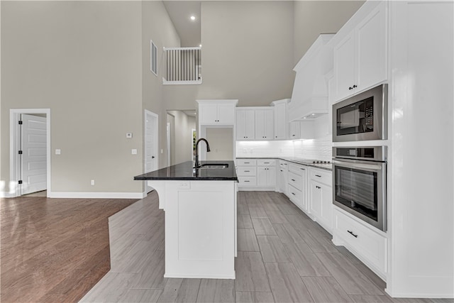 kitchen featuring sink, a towering ceiling, black appliances, and a center island with sink