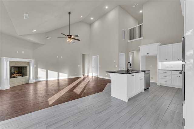 kitchen featuring ceiling fan, high vaulted ceiling, an island with sink, light hardwood / wood-style floors, and white cabinets