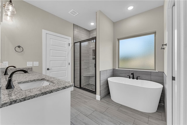 bathroom with vanity, separate shower and tub, and tile walls