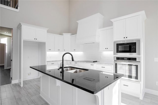kitchen with a towering ceiling, tasteful backsplash, a sink, white cabinets, and black appliances