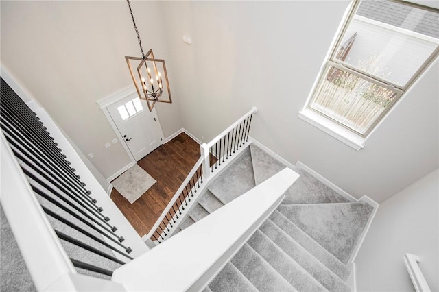 stairway with baseboards, a towering ceiling, wood finished floors, and a notable chandelier