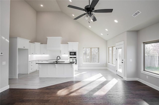 kitchen with white cabinets, stainless steel oven, built in microwave, and high vaulted ceiling