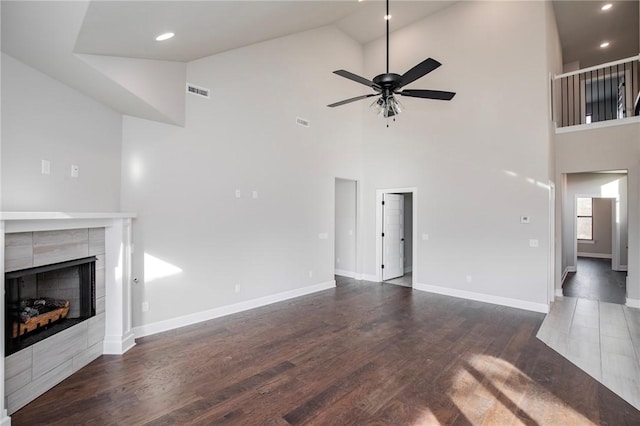 unfurnished living room featuring high vaulted ceiling, a tiled fireplace, a ceiling fan, wood finished floors, and visible vents