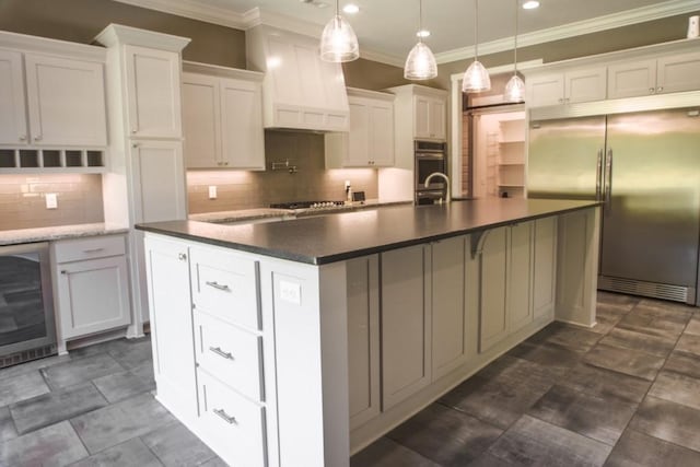 kitchen with a kitchen island with sink, white cabinets, wine cooler, appliances with stainless steel finishes, and decorative light fixtures