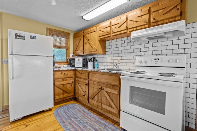 kitchen with light stone countertops, light wood-type flooring, sink, white appliances, and a textured ceiling