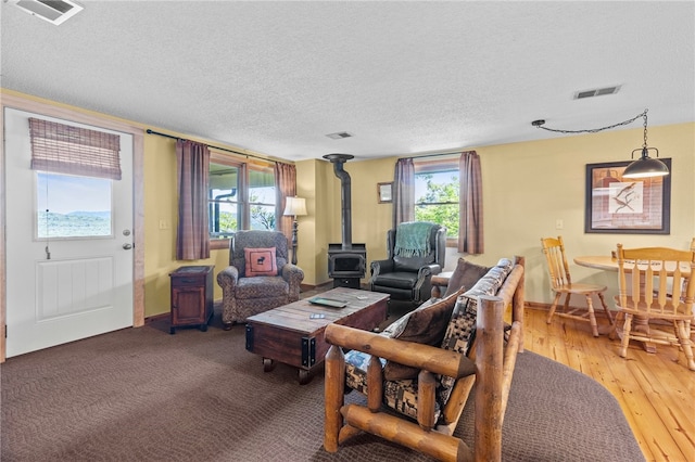 living room with wood-type flooring, a wood stove, and a textured ceiling