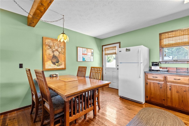 dining area featuring beam ceiling, light hardwood / wood-style flooring, and a textured ceiling