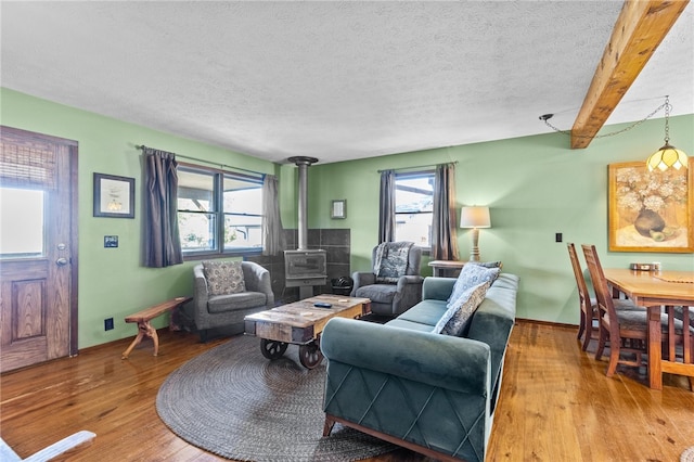 living room with wood-type flooring, beamed ceiling, a wood stove, and a textured ceiling