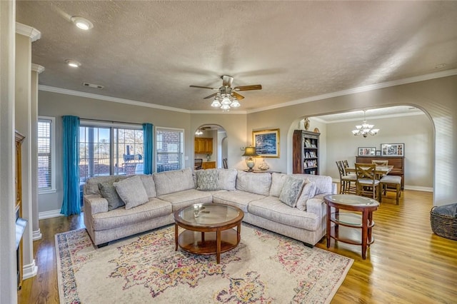 living room with light wood-type flooring, a textured ceiling, ceiling fan with notable chandelier, and crown molding