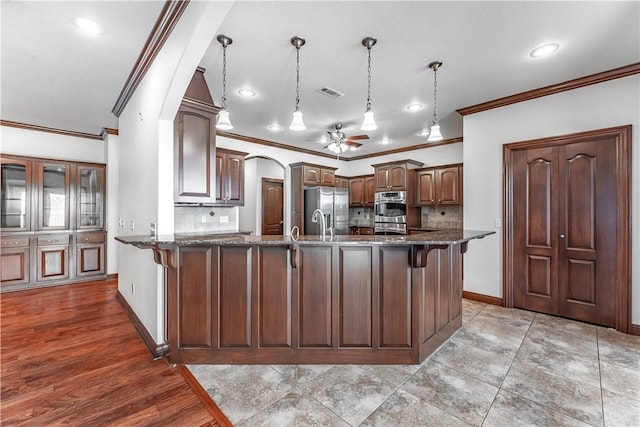 kitchen with stainless steel appliances, tasteful backsplash, an island with sink, decorative light fixtures, and ornamental molding