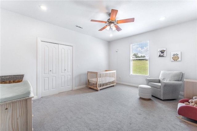 carpeted bedroom with ceiling fan, a closet, and a nursery area