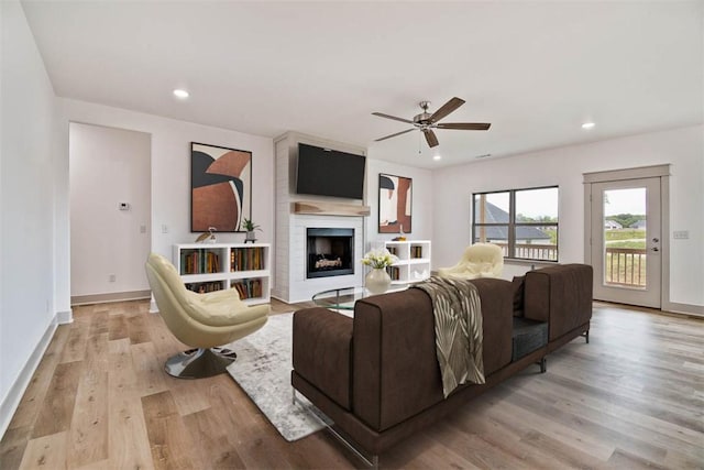 living room with a fireplace, light wood-type flooring, and ceiling fan