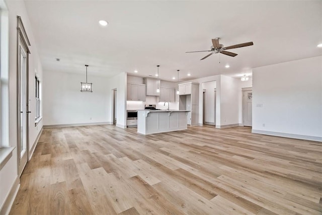 unfurnished living room featuring sink, ceiling fan with notable chandelier, and light hardwood / wood-style flooring